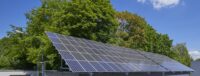 Dach-PV-Anlage vor grünen Laubbäumen. Photovoltaik für Unternehmen.